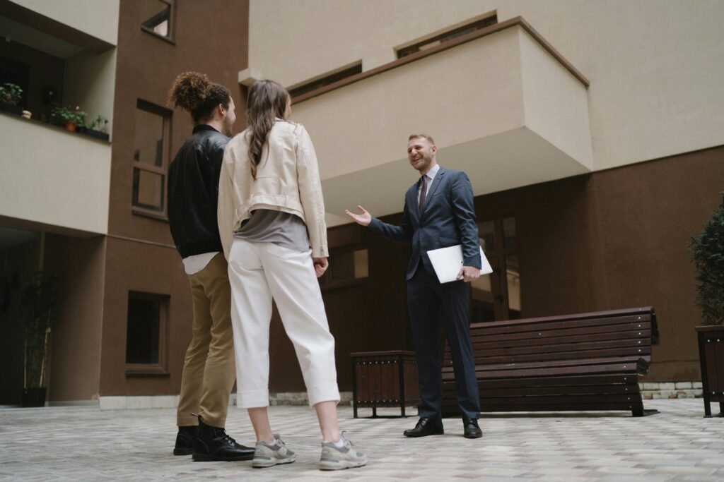 A realtor converses with a couple in a modern apartment courtyard.